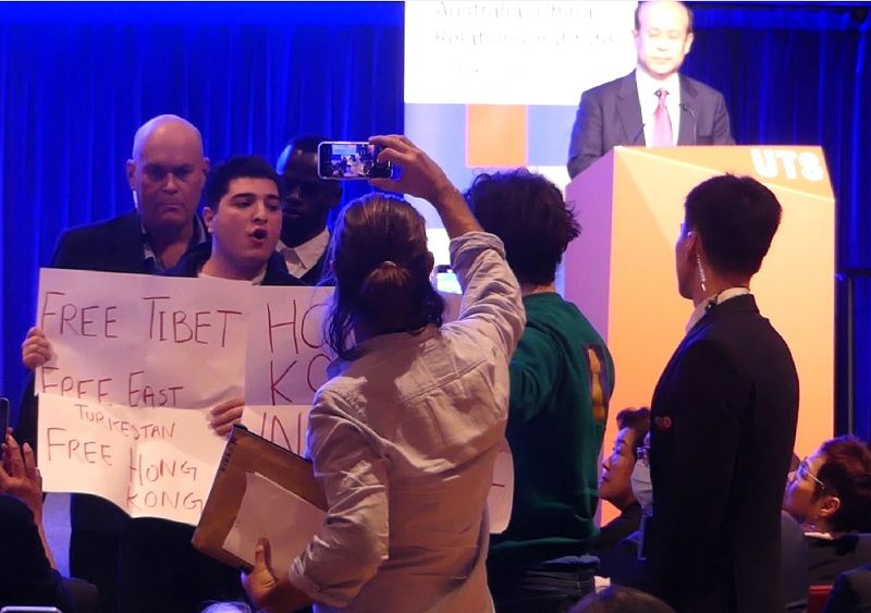 中國駐澳洲大使肖千（台上演講者）日前於雪梨科技大學（UTS）發表演說，過程中多次有抗議人士高喊口號譴責中國政府壓迫人權，導致肖千發言先後被打斷至少10次以上