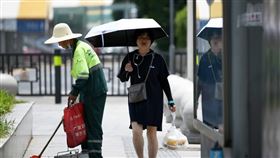 中國氣象局指出，21日起新一波的高溫天氣將影響全中國超過17個省市區，部分南方城市的體感溫度達攝氏60度。圖為江西南昌市，民眾在烈日下撐傘步行。（圖／中新社）
