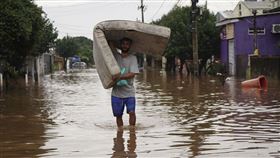 巴西南部發生嚴重洪患，圖為一名男子扛著床墊，涉水走過遭豪雨淹沒的街道。（圖／美聯社／達志影像）