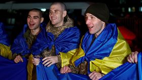 俄羅斯與烏克蘭在跨年夜前交換300多名戰俘，有許多烏克蘭軍人披著藍黃色相間的烏克蘭國旗。（圖／路透社／達志影像）