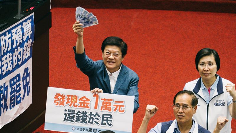 普發現金三讀後還拿著一萬元,笑得很開心,與綠營高舉反對標語形成兩樣情。(圖/記者楊士誼攝影)