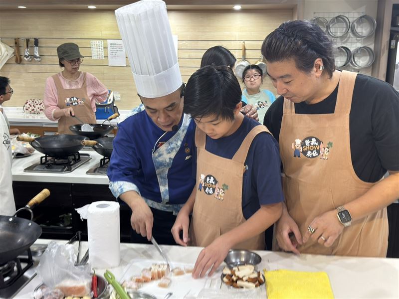 客家料理大廚郭敏昌阿全師（左一），現場指導參與的爸爸與小朋友製作道地客家小炒，透過親子共廚活動傳遞家的溫度與傳統飲食文化。(圖/大同區公所提供)