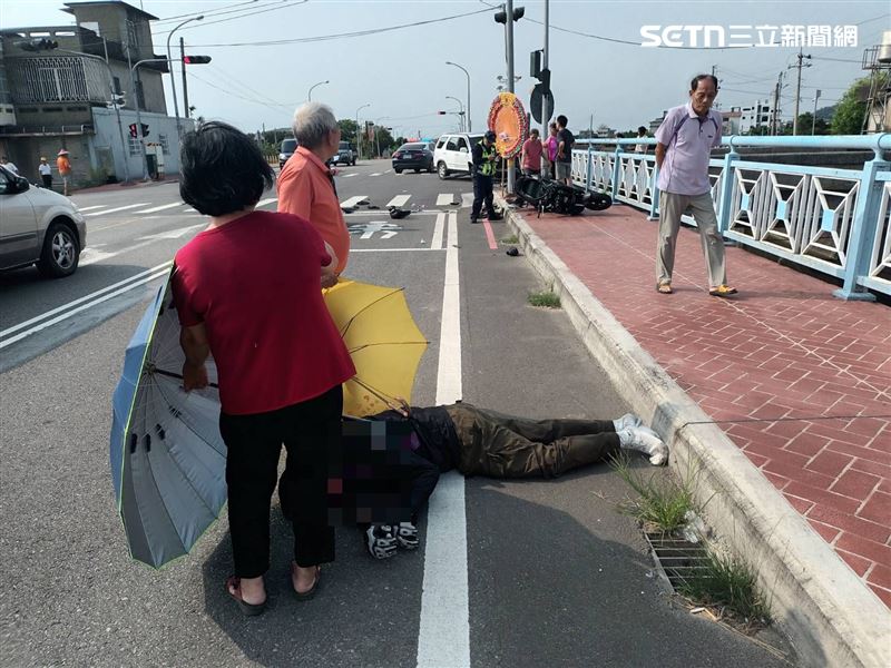 車禍發生後騎士倒地,附近的阿公阿嬤幫他撐傘等待救護車抵達。(圖/翻攝畫面)
