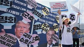 南韓總統李在明訪日、美前夕，民間團體在首爾一面手舉著有川普和石破茂照片的手牌，一面高呼主權與和平。（圖／美聯社／達志影像）