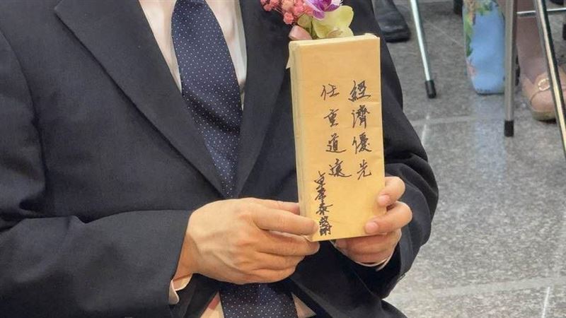 行政院長卓榮泰親手將一份牛皮紙包裝的小禮物交給新任經濟部長龔明鑫,包裝上寫著「經濟優先、任重道遠」八字箴言。龔明鑫笑稱「本來以為是糖果,結果好像是一支筆」,幽默化解媒體追問,也展現輕鬆一面,緊張莊重的典禮現場因此添上幾分趣味。(圖/記者師瑞德攝影)
