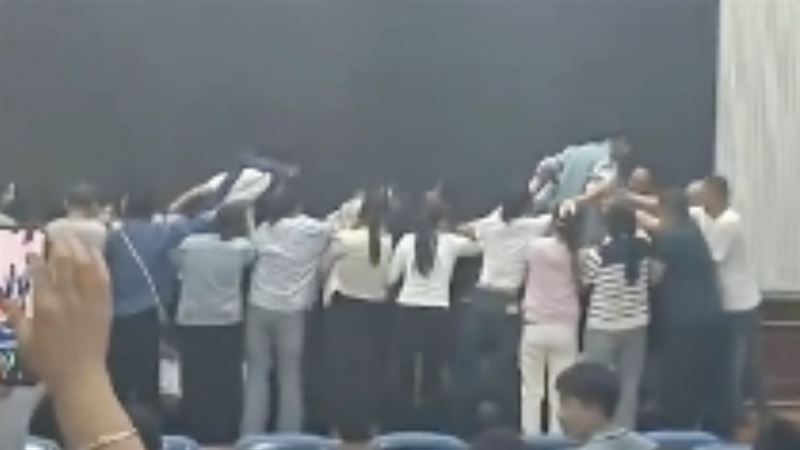 多名家長跪成一排，矇眼的學生在攙扶下依序踏過家長背部。（圖／翻攝自極目新聞）