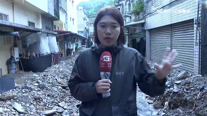 記者後方都是土石流沖刷下來的土石