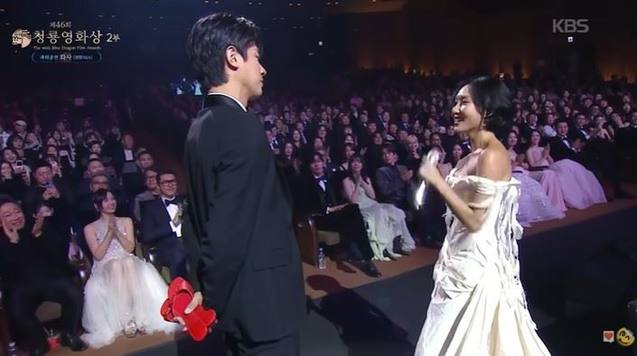 華莎（右）演唱《Good Goodbye》時，看見演員朴正民（左）正背著手、拿著一雙紅色高跟鞋，像是等待「交接任務」般站在原地，氣氛瞬間變得像小劇場。（圖／翻攝自KBS Entertain YT）