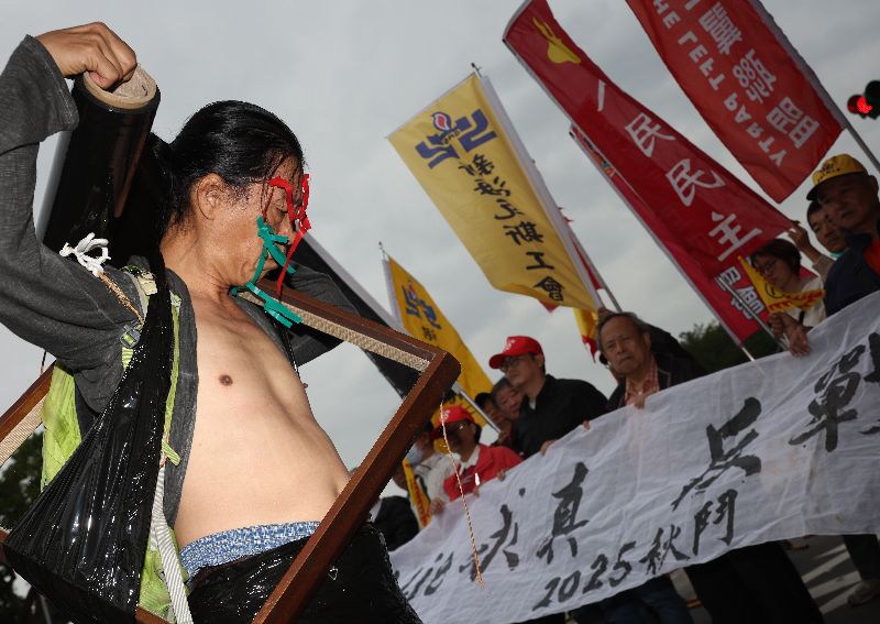 2025秋鬥行前記者會25日上午在總統府前凱達格蘭大道舉行，行為藝術家曾啟明（前左）於會中透過行為藝術表達反戰訴求，呼籲政府應將執政重心放在社會改革，讓人民過好生活、堅守和平立場