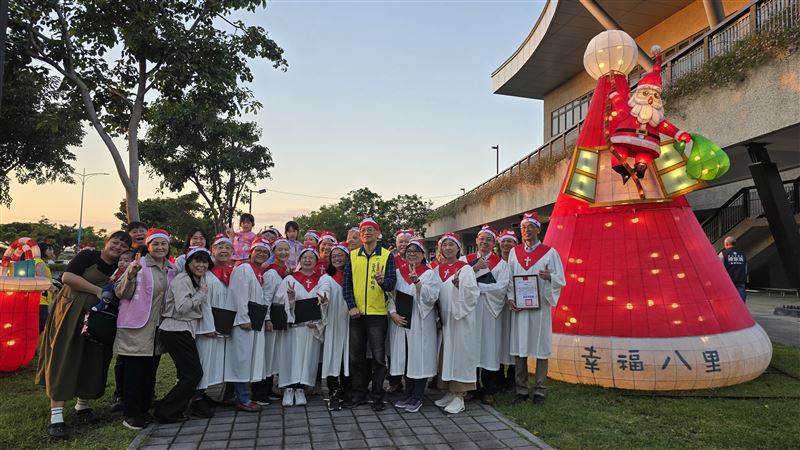 2025八里聖誕今天傍晚幸福點燈，巨型耶誕帽燈飾現身，教會獻唱聖歌，民眾熱情參與。（圖／公所提供）