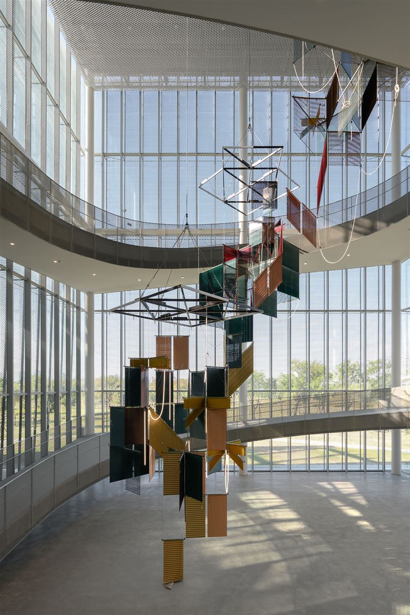 梁慧圭 ( Haegue Yang )，《流動奉獻－樹蔭三合》，2025，鋁製百葉窗、粉末塗層鋁懸掛結構、鋼纜、LED燈管、雷射照明、開關電源、無線模組、電線，2,362 x 1,086 x 1,086公分，藝術家自藏，臺中市立美術館委託創作。（圖／臺中市立美術館提供）