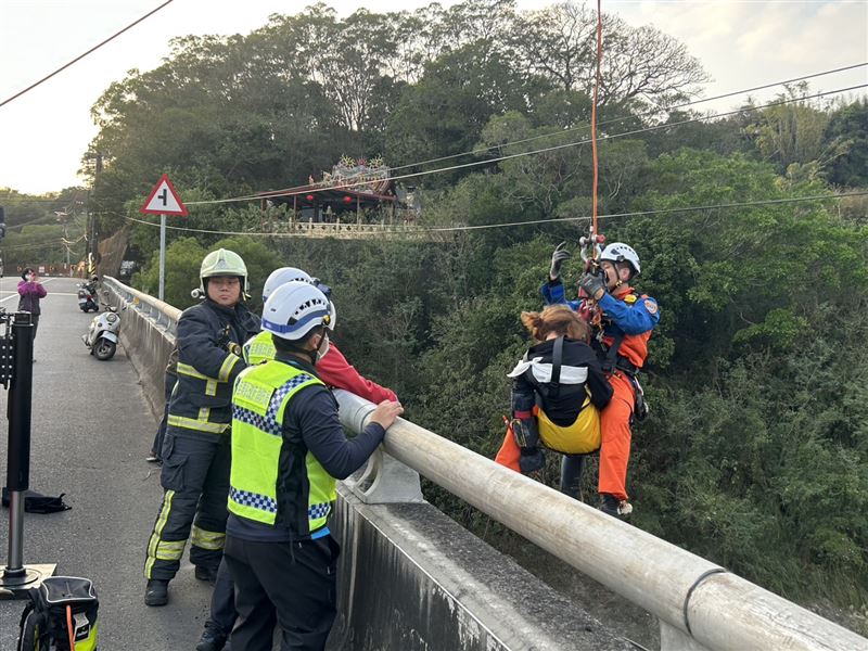 消防人員垂降至河床上,以三角吊帶攜帶李女上橋。(圖/翻攝畫面)