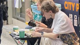 兩個老外蹲坐在超商外頭，把傘架當餐桌，吃起剛買來的食物。（翻攝「活網缺愛集散地4.0 」臉書社團）