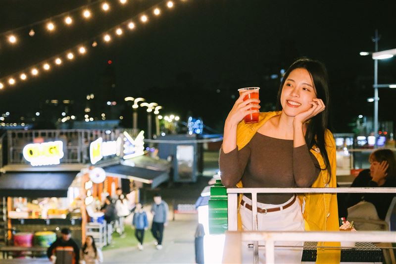 稻埕碼頭夜色中，旅人倚欄小飲，燈串與河岸光影交織出城市煙火氣。（圖／翻攝畫面）