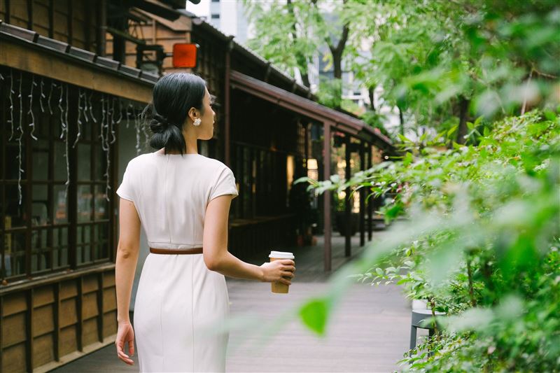 午後的榕錦時光生活園區，旅人手捧咖啡行走於木造廊道間，老屋與綠蔭交織，咖啡香在光影中流動。（圖／翻攝畫面）