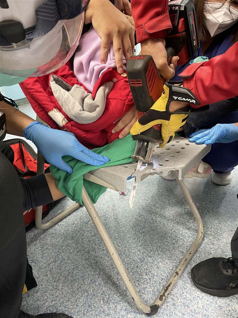 2歲女童因好奇把手指插入塑膠椅的洞洞拔不出來，因疼痛大哭，救護人員小心翼翼鋸開椅面。(圖／翻攝畫面)