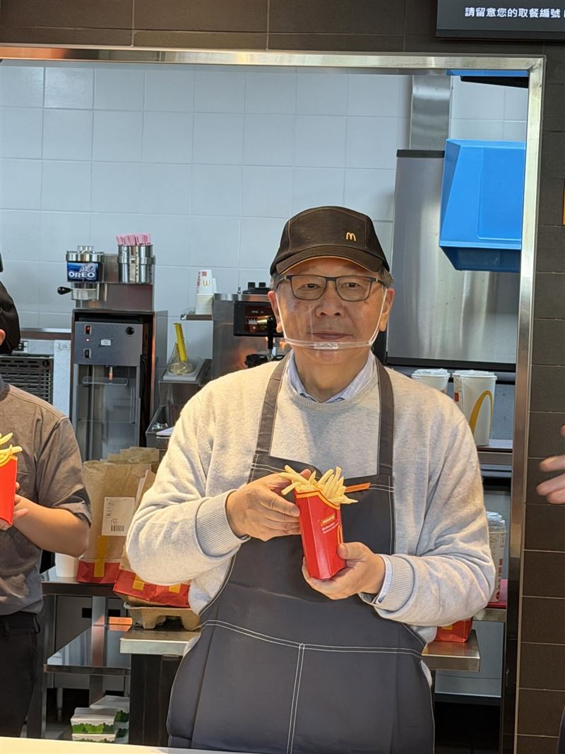 蔡力行站在麥當勞櫃檯後方，身穿圍裙、戴著帽子，手裡拿著一份薯條，神情輕鬆、笑容自然，整體畫面不僅可愛，還意外地毫無違和感。（圖／聯發科提供）