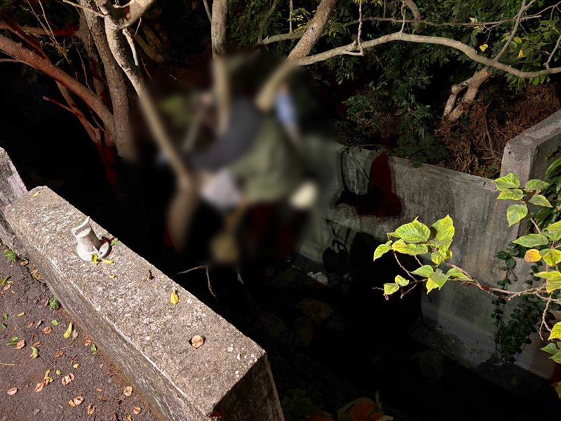 婦人騎車時因不明原因發生撞擊，人噴飛至路旁3公尺深圳溝，隨後婦人墜落「倒頭栽」卡在溝中的樹幹上，呈現倒掛U字型。（圖／民眾提供）