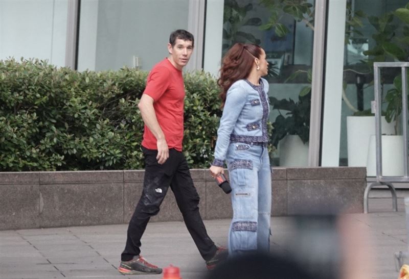 延遲了24小時，美國攀岩傳奇艾力克斯霍諾德（Alex Honnold）25日早晨8時30分左右，身穿招牌紅色T恤，神情輕鬆地出現在台北101大樓。面對現場早已擠爆的粉絲與媒體，他露出招牌的靦腆微笑，親切地揮手致意，完全看不出即將進行一場「玩命挑戰」的緊張感。（圖／記者鄭孟晃攝影）