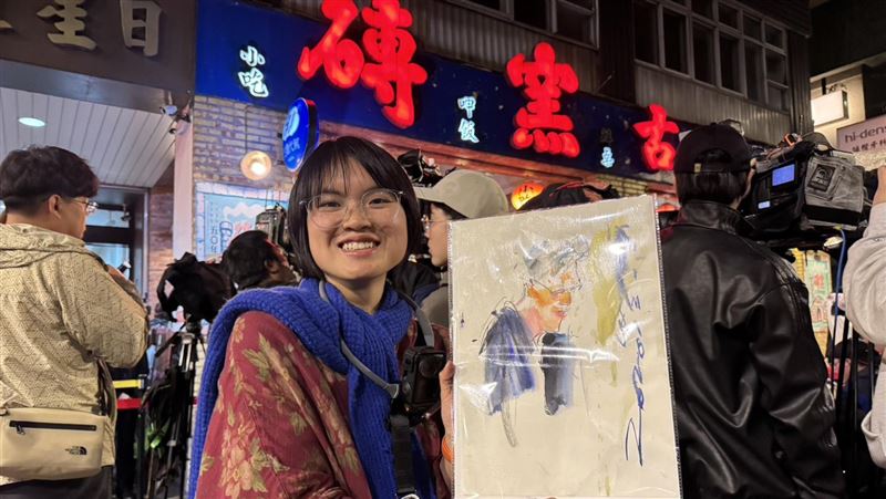 輝達執行長黃仁勳今晚在「磚窯」餐廳宴客,吸引大批粉絲包圍。現場一位街頭速寫畫家吳沁頤,自備板凳在喧鬧中即席作畫,以驚人速度捕捉黃仁勳神韻。她聽從《三立新聞網》記者的「戰略建議」調整卡位動線,果然成功等到黃仁勳現身互動,順利在剛完成的畫作上獲得親筆簽名,圓滿達成心願。(圖/記者余國棟攝影)