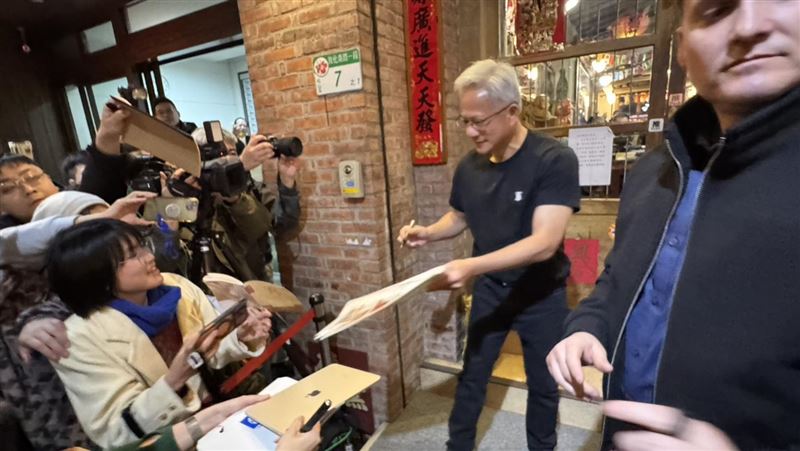 輝達執行長黃仁勳今晚在「磚窯」餐廳宴客,吸引大批粉絲包圍。現場一位街頭速寫畫家吳沁頤,自備板凳在喧鬧中即席作畫,以驚人速度捕捉黃仁勳神韻。她聽從《三立新聞網》記者的「戰略建議」調整卡位動線,果然成功等到黃仁勳現身互動,順利在剛完成的畫作上獲得親筆簽名,圓滿達成心願。(圖/記者余國棟攝影)