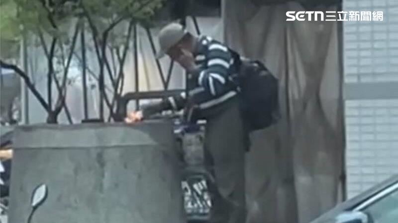 一名揹著大後背包的男子，選在清晨時分於店外花圃蹲下，點燃白紙「助火」燃燒。更詭異的是，當火勢熄滅後，他竟突然用頭部猛力撞擊牆壁，讓目擊的住戶嚇壞。(圖/翻攝畫面)