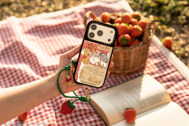 「迪士尼小熊維尼莓果手機吊飾」採用綠色腕帶與精緻草莓墜飾，細膩還原森林採摘果實的童趣瞬間。（圖／CASETiFY提供）