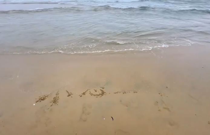 一道浪花精準地拍向「不想上班」四字,待潮水退去後,沙灘上的殘餘字跡竟奇蹟般地組成了「小心一點」。(圖/翻攝自X平台 @yingtan04410735)