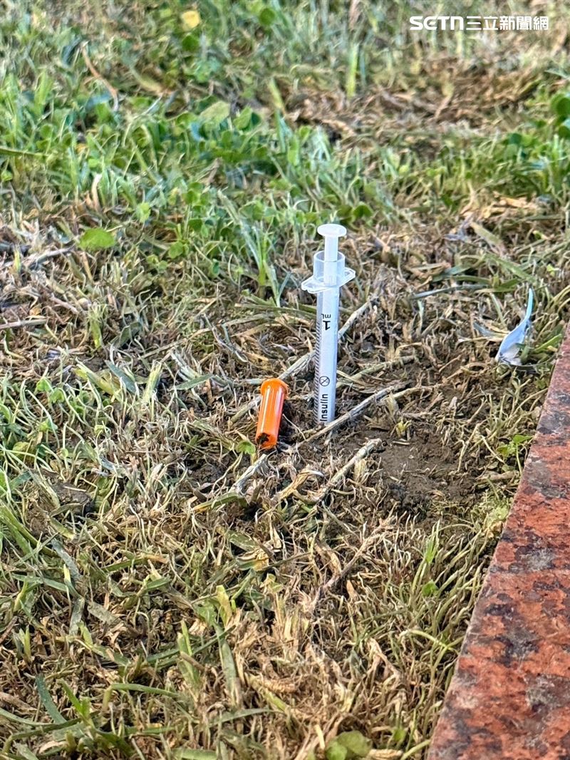 警員在案發現場旁花圃尋獲一支安非他命注射針筒。（圖／翻攝畫面）