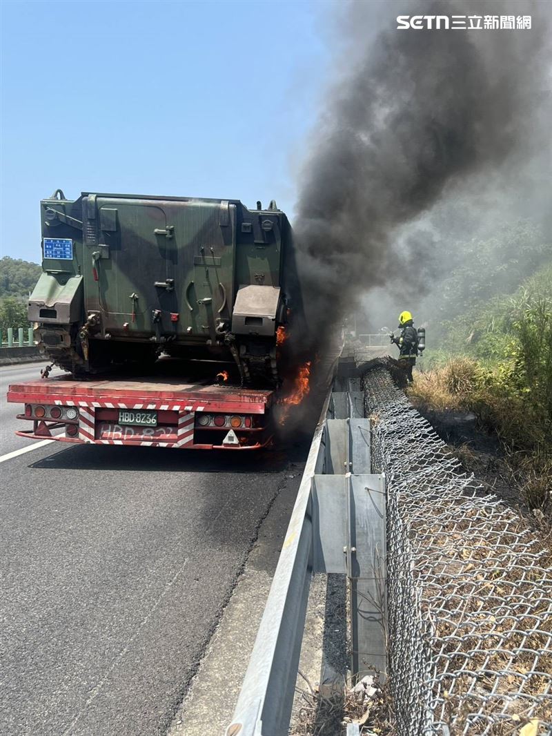 一輛載運國軍裝甲車的拖板車，在行駛途中底盤突然竄出黑煙並起火燃燒，火勢一度延燒至上方的軍用裝甲車。（圖／翻攝畫面）