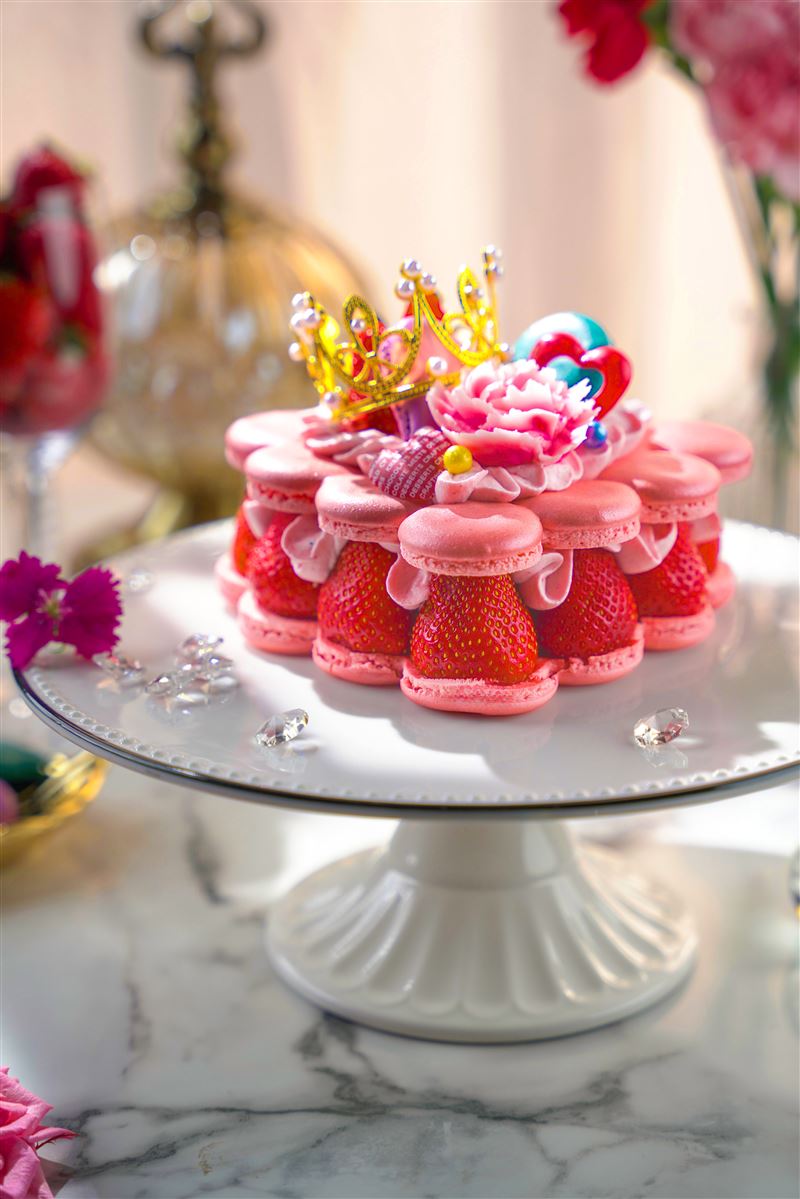 君品酒店全新推出「馨心相映」草莓馬卡龍蛋糕售價1,380元，以粉紅馬卡龍環繞並點綴皇冠與康乃馨糖花，內餡別出心裁以白豆沙揉合大湖草莓與白蘭姆酒。（圖／飯店旅宿業者提供）