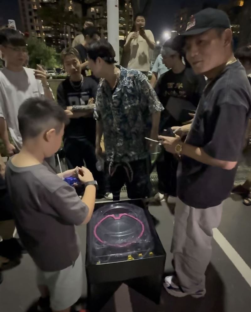 春風拿著改裝過的戰鬥陀螺跟小朋友對戰，吸引大批民眾圍觀。（圖／翻攝自Threads @911_eo）