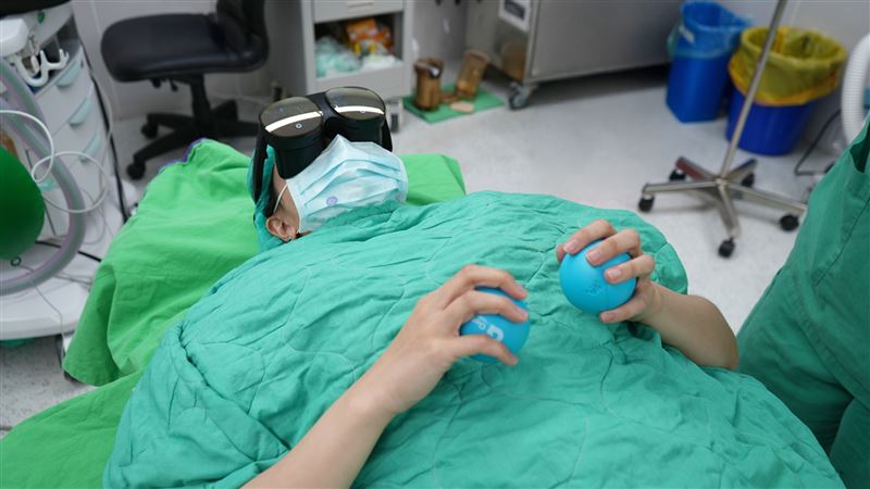 病人戴著VR眼鏡、蓋溫熱毯、聞香氛味、捏壓力球,一邊數數字…等方式降低術前焦慮。(圖/臺北醫院提供)