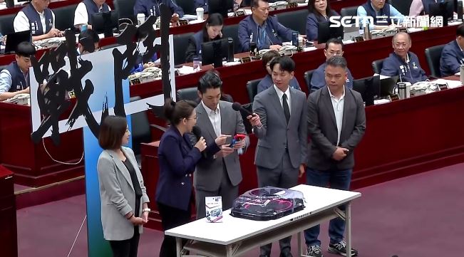 民眾黨團送蔣萬安戰鬥陀螺，結果遞過去時陀螺掉下來（圖／翻攝畫面）