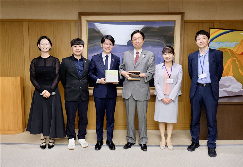 高雄市青年局長林楷軒（左三）率團拜會日本熊本縣知事木村敬（右三），致贈高雄青創基地業者「大雄的木作世界」客製化手工木屐筆，熊本則以當地特製伴手禮回贈致意。（圖／高雄市政府青年局提供）