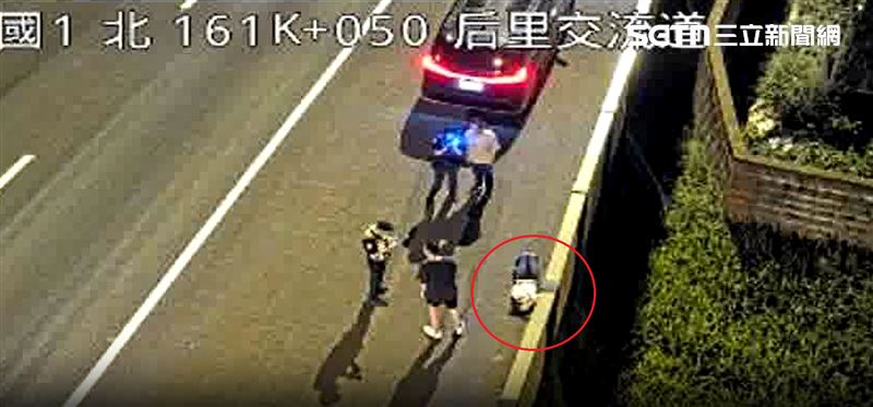 國道上的路肩正躺著一名女子頭部重創流血,國道員警一邊手持指揮棒警戒後方呼嘯而過的大型貨車。(圖/翻攝畫面)
