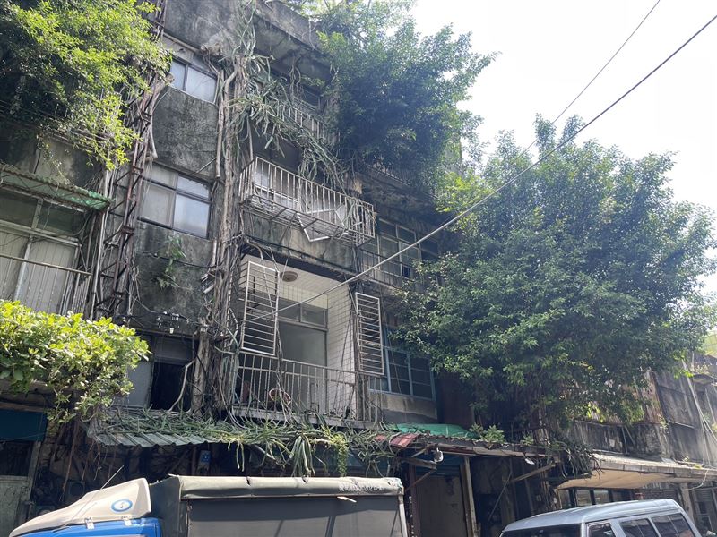 在寸土寸金的信義區，五分埔遷建基地卻保留民國44年安置時的斑駁樣貌，外牆縫隙甚至攀出樹木藤蔓、盤根錯節，與一街之隔的信義豪宅群形成強烈對比，官方文件因此正式定名為「五分埔窳陋社區都市更新案」。（圖／台北遷建提供）