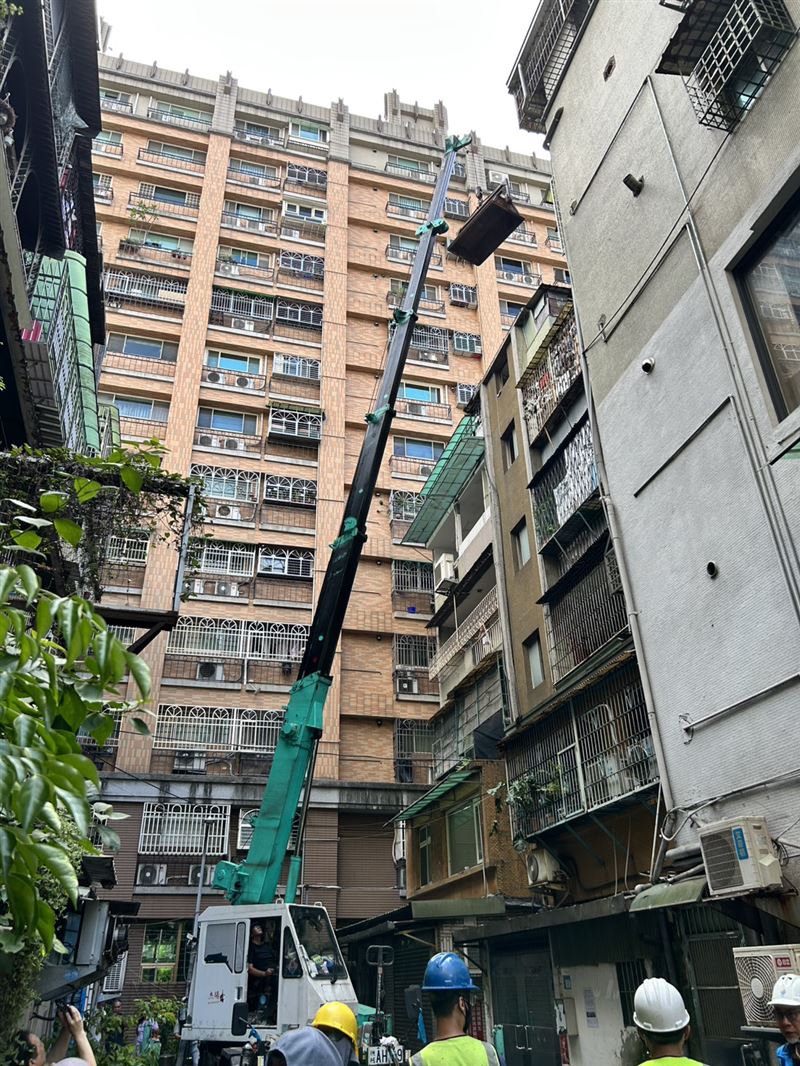 進場困難,本次採取高空吊掛方式將頂樓雜物一批批吊下,吊運路徑周邊卻布滿電纜,鄰近住家也設有遮雨棚。工作人員操作吊掛時必須精準控制,每一步都得避開障礙物(圖/新北市政府提供)