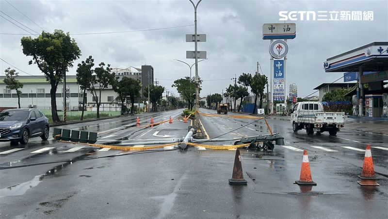 高雄大寮區光明路三段、大倫加油站外分隔島上一支紅綠燈桿禁不起強風遭連根拔起,呈現T字型趴倒在地,佔據兩個車道。(圖/翻攝畫面)