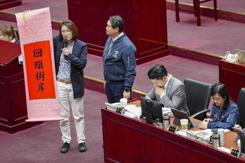 台北市議會日前進行市長施政報告質詢,民進黨台北市議員林延鳳(左)贈送台北市長蔣萬安(右2)寫有「回頭樹岸」字樣的掛軸,質疑台北市政府任意移除樹木,要求市府重視樹木保護