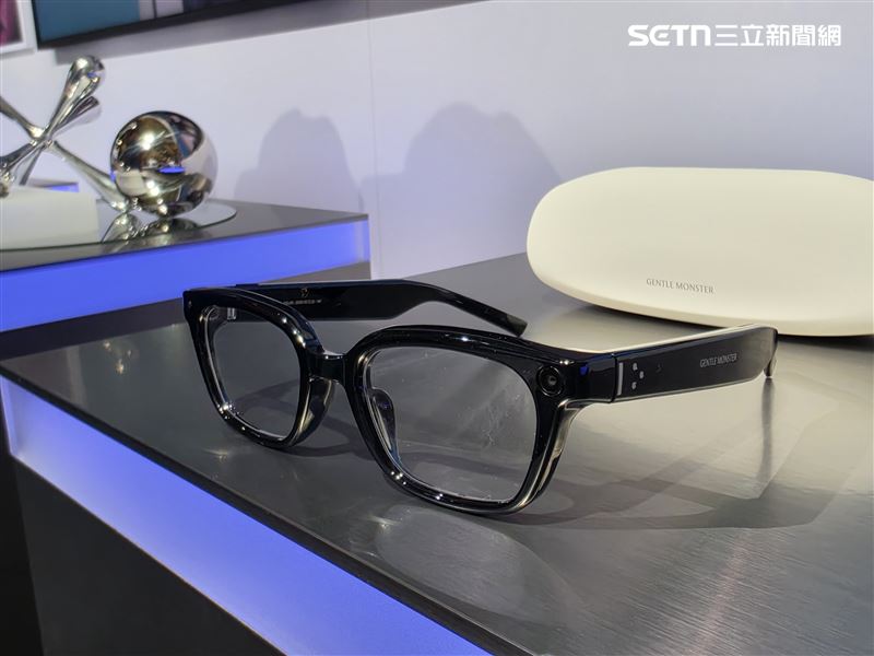 視線轉向另一款主角「Warby Parker」，黑色方框光學眼鏡以斜角之姿平放展示台上，與白色「GENTLE MONSTER」收納盒相互映襯，畫面層次分明。鏡框左側同樣藏有鏡頭狀裝置，並標註「GENTLE MONSTER」字樣，低調中透出科技感。圖／三立iNEWS）