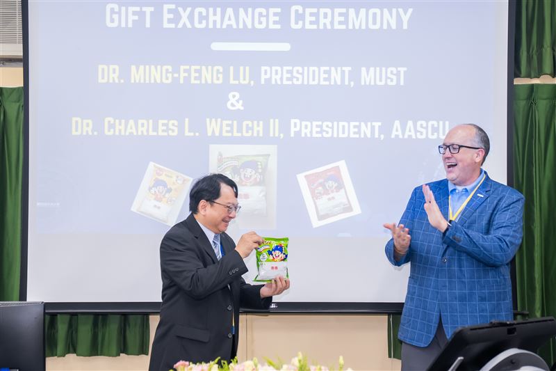 明新科大校長呂明峯(左)致贈綠色包裝「乖乖」予AASCU主席 Dr. Charles L. Welch II(右),並分享臺灣科技圈祈求機台「乖乖運轉」的趣味文化