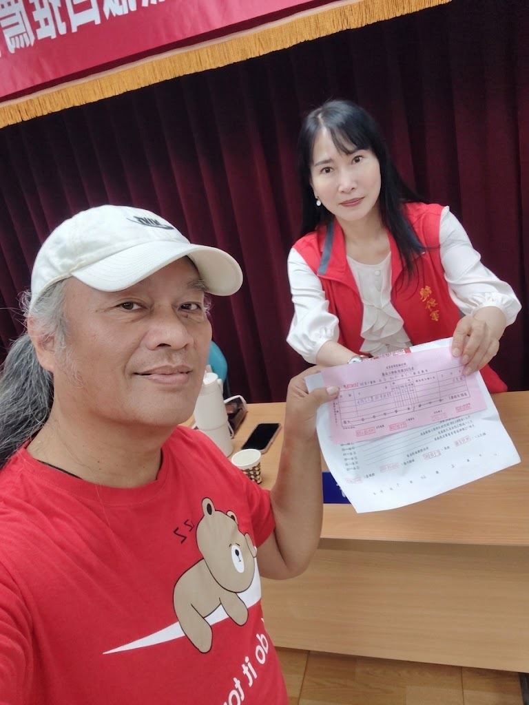 林世偉身穿紅色熊熊T恤手持登記收據,與選委會副主委美玲姐姐及工作人員合照。(圖/翻攝自林世偉臉書)