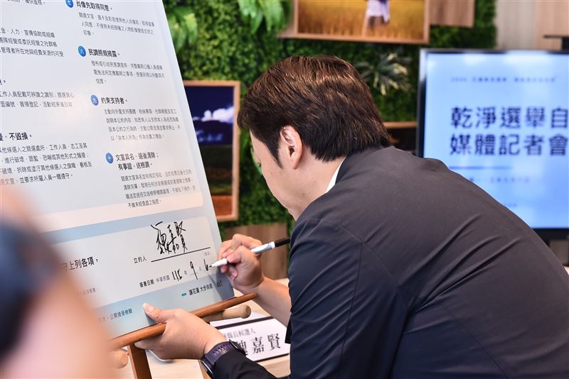 魏嘉賢在大型公約看板簽下名字,正式簽署包含10項內容的「乾淨選舉自律公約」。(圖/翻攝畫面)