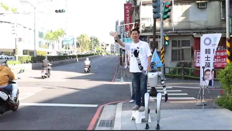 民眾黨新北市議員候選人邸聖德在新店北新橋頭，帶著人形機器人一同向自新店進台北市的通勤民眾「揮手」拜票。（圖／翻攝自邸聖德臉書）