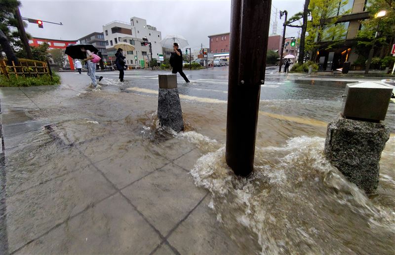 受颱風杜鵑帶來的暴雨影響,鎌倉市人們小心翼翼地穿過被水淹沒的十字路口。(圖/美聯社/達志影像)