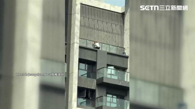 穿著白色襯衫的男子沒戴工程帽,人還蹲在高樓陽台外側一手搭著欄杆維持平衡
