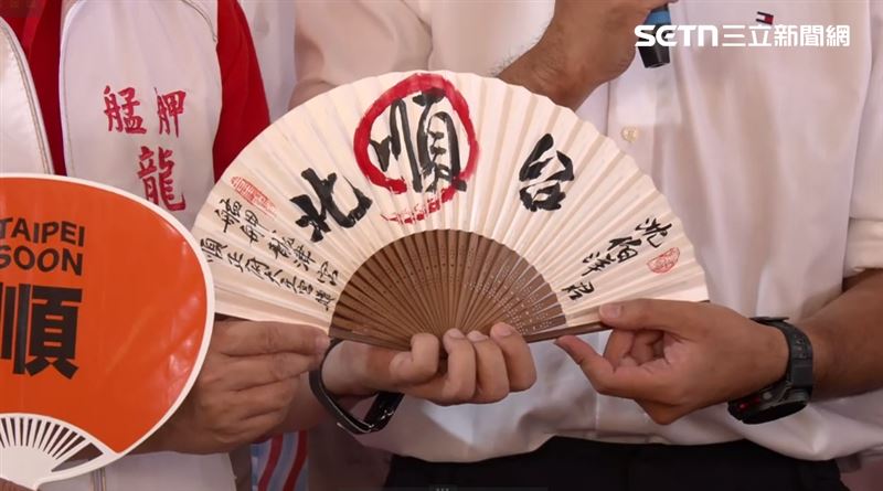 沈伯洋從龍津宮主委林政平手中接下一把寫有「沈伯洋君 台北順」的扇子,「順」字更用紅色圈起強調。沈伯洋致詞表示,除了希望台北可以順起來,其實有很多事情都應該要順起來。(圖/翻攝畫面)
