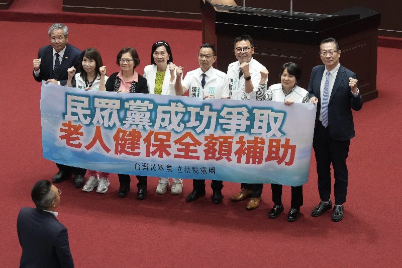 立法院會16日三讀修正通過老人福利法第22條條文,近1年綜合所得未達申報標準或綜所稅稅率未達20%的相對經濟弱勢長輩,由中央主管機關補助全額健保費。民眾黨立院黨團在議場中舉標語慶祝